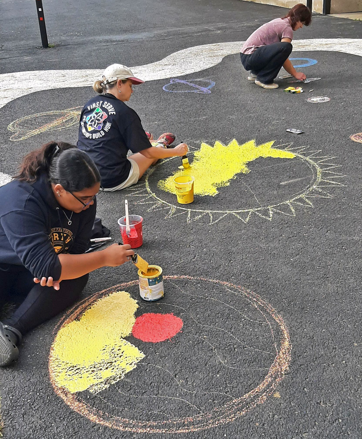 Participants paint yellow designs on the ground. 